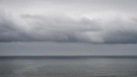 Dark dramatic storm clouds hanging low over a calm ocean Stock Photos