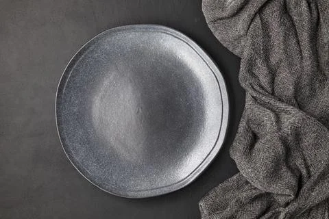 Dark empty handmade ceramic plate and kitchen towel on a black concrete table Stock Photos