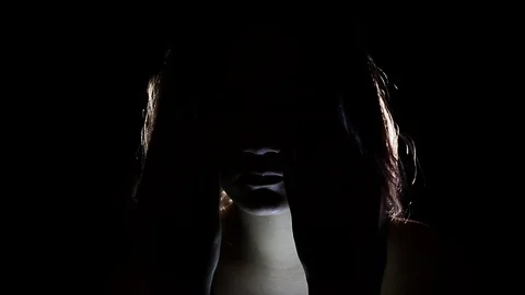 Dark figure covering its face with light shining thru Stock Footage 122357046