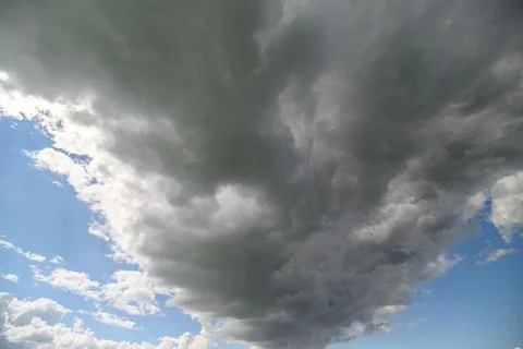 Dark gray clouds merge with soft white puffs against a backdrop of vibrant bl Stock Photos