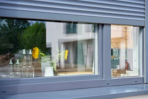 Dark gray roller shutter shades the upper part of a kitchen window, with sunf Stock-Fotos