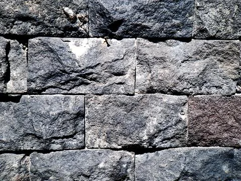 Dark gray stone wall constructed of rough-hewn blocks, creating a rugged, t.. Stock Photos