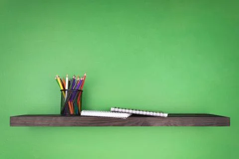 On a dark green background a shelf on which are two notebooks and a clerical Stock Photos