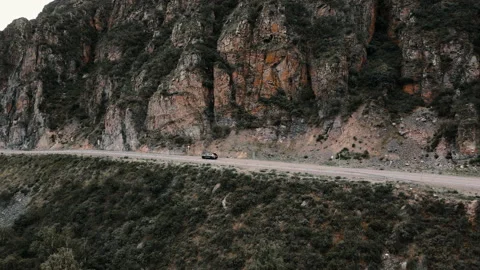 Dark grey car drives through narrow road in the mountains. Drone footage Stock Footage 166060819