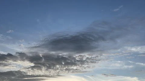 Dark grey fluffy clouds spreading across blue evening sky with soft sunligh.. Stock Photos