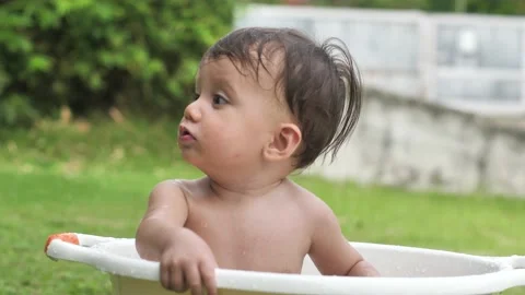 A dark-haired and cute child splashes his hand in the water sitting in the basin Stock Footage 189057013