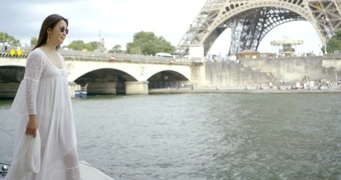 A dark-haired Asian middle-aged woman walks in Paris against a bridge, along the Stock Footage 113940640