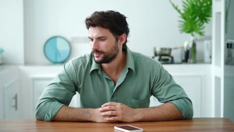 Dark-haired bearded Caucasian man in his 30s, sits at a wooden table in the Stock Footage 219547012