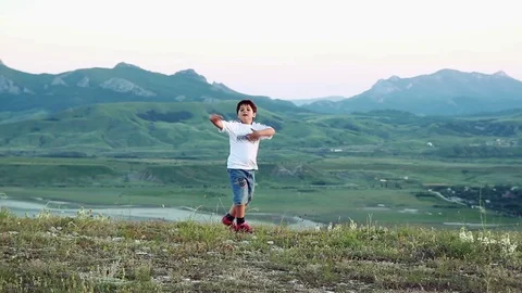 Dark-haired boy dancing on the background of mountains Stock Footage 76470013