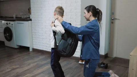 Dark-haired female parent helping her kid put on a school backpack indoors. Stock Footage 345917327