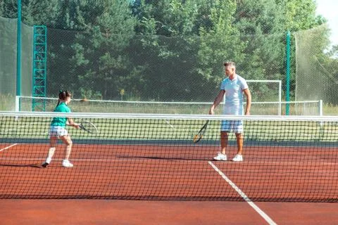 Dark-haired girl running while playing tennis with daddy Stock Photos