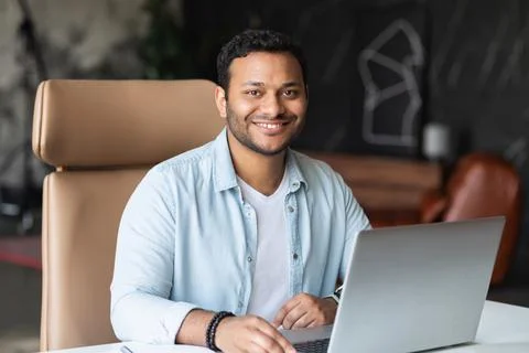 Dark-haired indian handsome guy wearing casual shirt using laptop Stock Photos