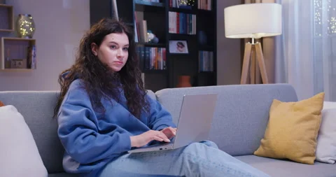 Dark haired lady working on wireless laptop while sitting on cozy couch at home Stock Footage 244143817