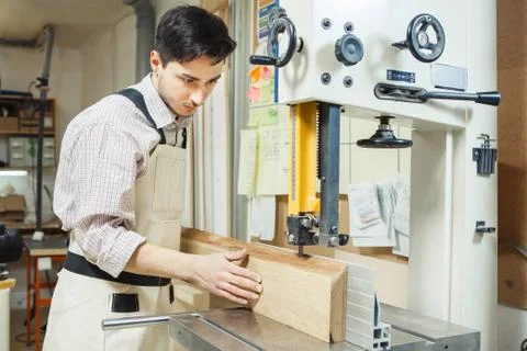 Dark-haired man holding timber on band saw Stock Photos