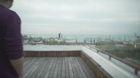 Dark haired man with journal in hand in casual clothes walking on wood rooftop l Stock Footage 132675472