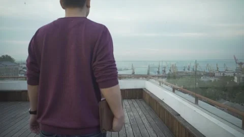 Dark haired man with journal in hand in casual clothes walking on wood rooftop l Stock Footage 132675478