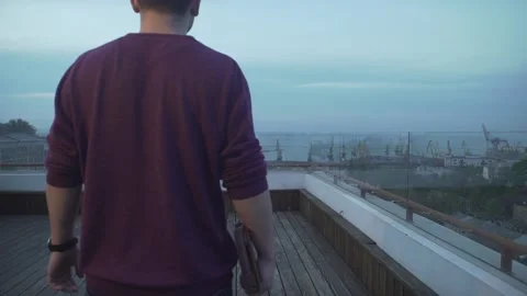 Dark haired man with journal in hand in casual clothes looking at harbor seascap 動画素材 132675528