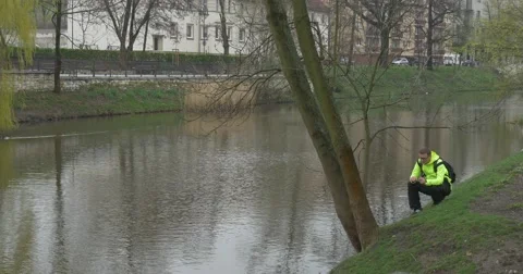 Dark-Haired Man Sits on Shore of a Small River Stock Footage 62186057