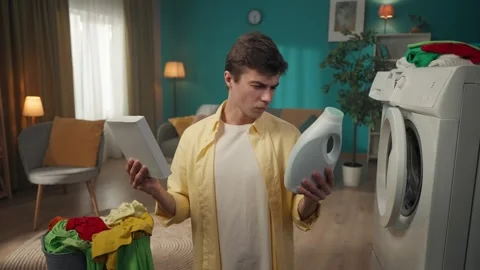 Dark-haired man sitting next to a washing machine and a landry basket, selecting Stock Footage 252386815