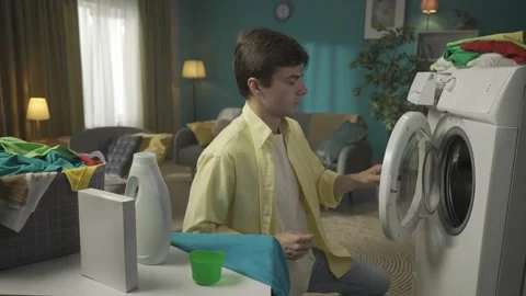 Dark-haired man sitting next to a washing machine, pouring a liquid detergent Stock Footage 252391020