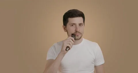 Dark-haired man with smooth skin arranges his beard with the help of an electric Stock Footage 232688175