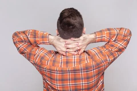Dark haired man standing backwards to camera, raised his arms, holding neck Stock-Fotos