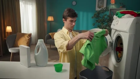 Dark-haired man standing next to a washing machine, unloading clean clothes Stock Footage 252389076