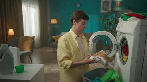 Dark-haired man standing next to a washing machine, unloading clothes that didn Stock Footage 252389579