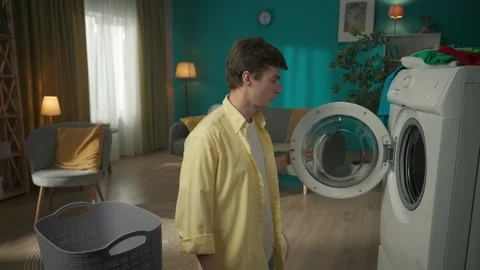 Dark-haired man standing next to a washing machine, unloading it. The clothes Stock Footage 252389803