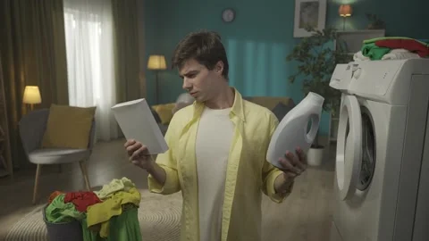 Dark-haired man standing next to a washing machine and a laundry basket Stock Footage 252390165