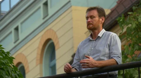 The Dark-Haired Man Stands on a Small Balcony Stock Footage 67553470