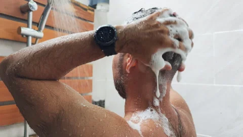 A dark haired man is thoroughly washing hair with shampoo standing in shower. Video stock 321858077