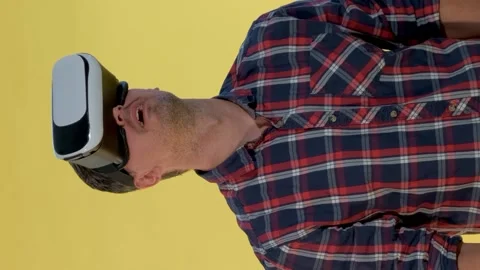 Dark-haired man using virtual reality glasses while standing against yellow Stock Footage 130182814