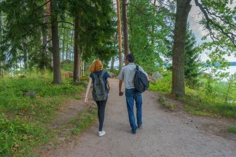 Dark-haired middle-aged man and red-haired young lady walk along forest road. Stock Photos