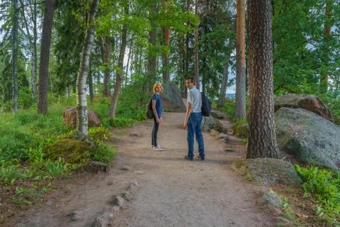 Dark-haired middle-aged man and red-haired young lady walk along forest road. Stock Photos