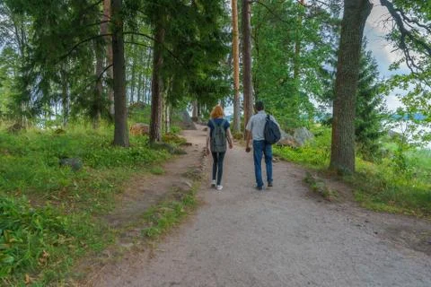 Dark-haired middle-aged man and red-haired young lady walk along forest road. Stock Photos
