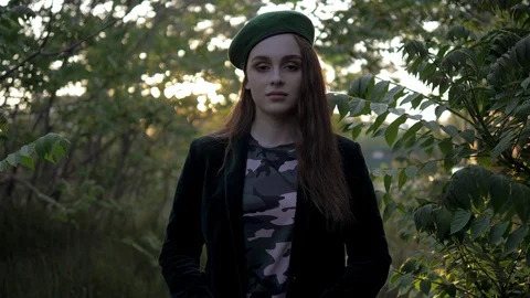 Dark haired model in beret poses by tree at evening sunlight Stock Footage 109154685