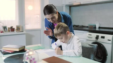 Dark-haired mother explaining school homework to her young son indoors. Видео 345917235