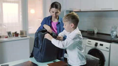 Dark-haired parent helping her kid pack a school backpack indoors. Stock Footage 345917294