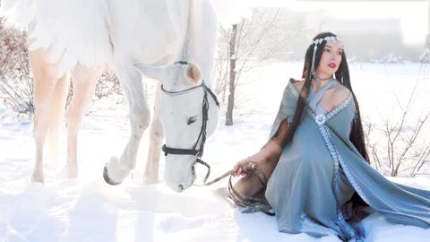 Dark-haired princess sitting in the snow in frosty weather, thoughtful serious Stock Footage 103595816