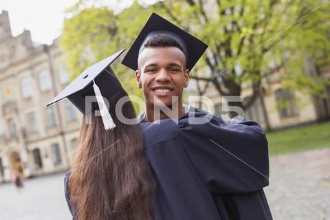Dark-haired student in mortarboard hugging her boyfriend Stock Photos