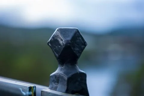 Dark hexagonal stone ornament mounted on metal rail with out-of-focus green a Foto stock