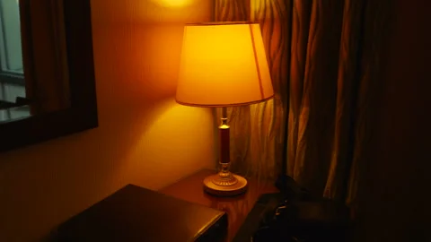 Dark hotel room lit by table shade lamp mirror on wall and curtained window Vídeo Stock 105672939