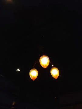 A dark interior with a decorative three-light chandelier casting amber glow a Stock Photos