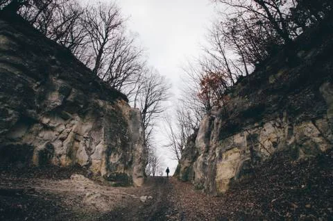 Dark landscape with man walking on path through canyon cliffs with trees Stock Photos