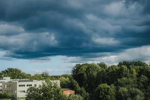 Dark, layered storm clouds tower over lush green trees. Stock Photos