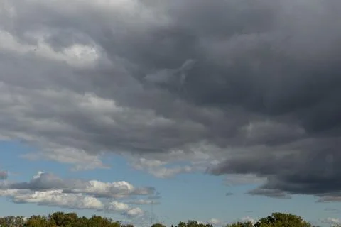 Dark, layered storm clouds tower over lush green trees. Stock Photos