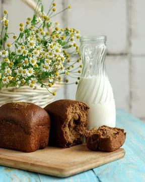 Dark loaf of rye bread and milk bottle on kitchen table. Light breakfast and Stock Photos