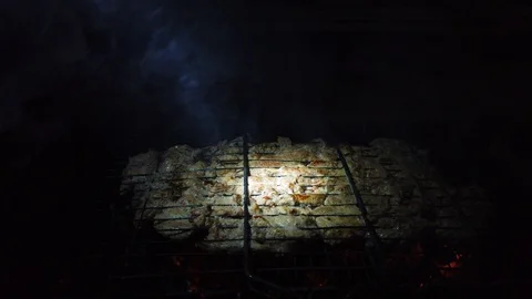 In the dark, meat is grilled on the grill in the rays of a flashlight. Stock-Footage 115898019