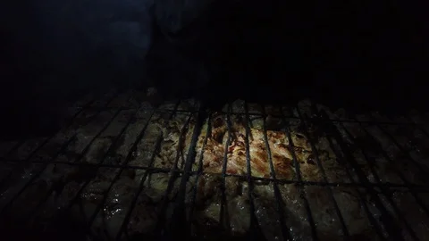 In the dark, meat is grilled on the grill in the rays of a flashlight. Vídeos de archivo 115898286